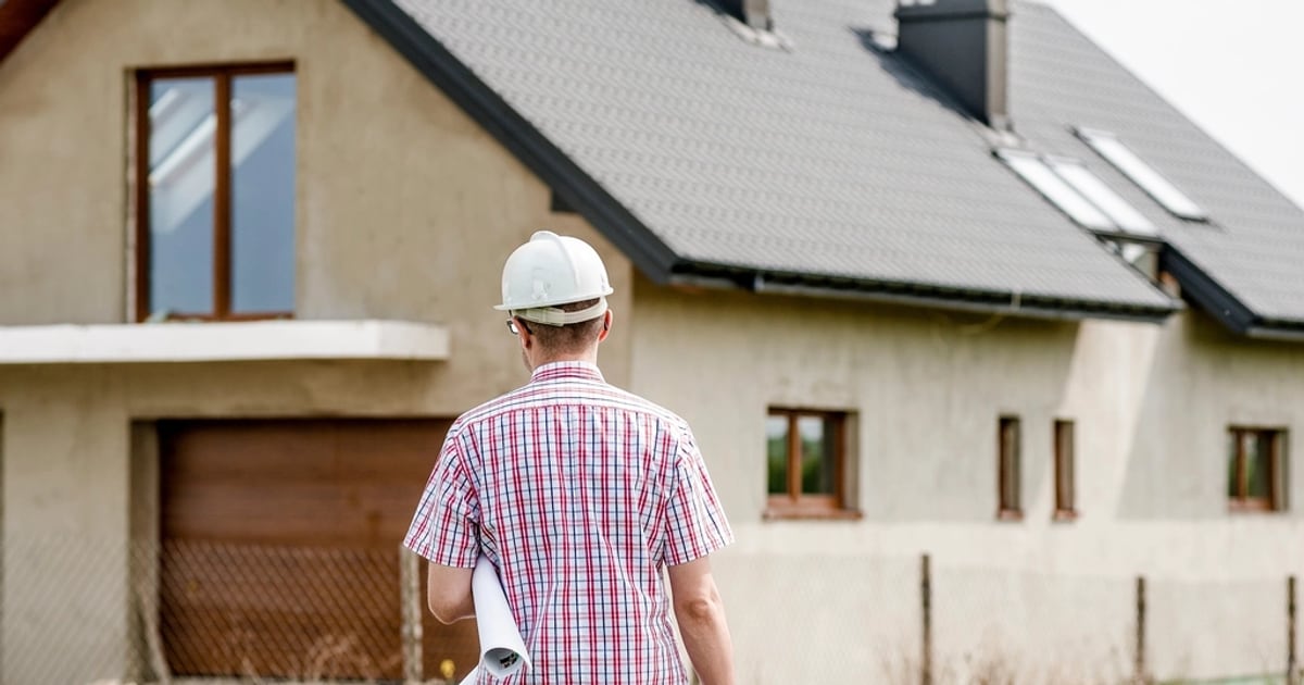Site engineer in a hard hat holding plans in front of a newly built house