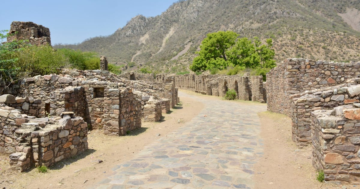 Old stone ruins and walls along a paved path below a rocky hillside