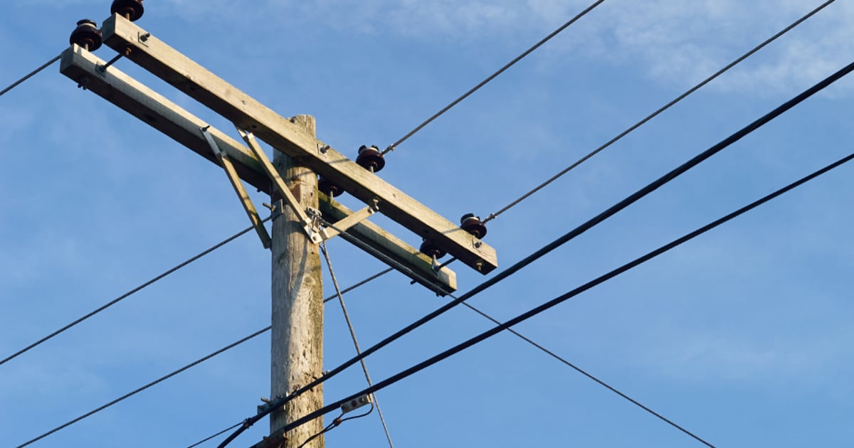Wooden electricity pole with overhead power lines against a blue sky